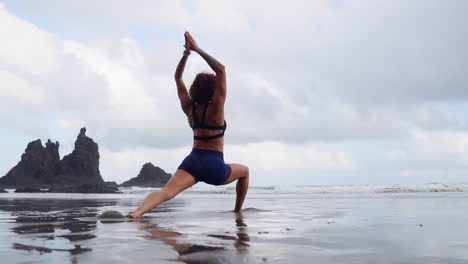 Captured-in-slow-motion,-a-young-and-slender-woman-engages-in-stretching-and-yoga-by-the-ocean's-edge,-her-gaze-fixed-into-the-distance