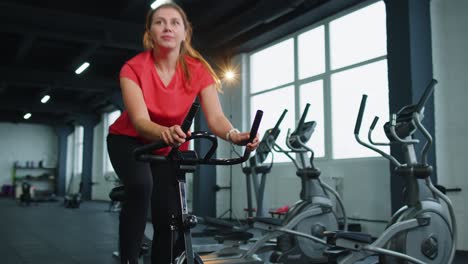 Athletic-young-woman-ride-on-spin-stationary-bike-training-routine-in-gym,-weight-loss-indoors
