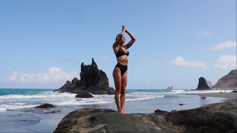 In-slow-motion,-a-young,-slender-woman-engages-in-yoga-while-standing-on-a-rock-by-the-ocean