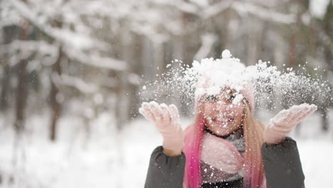 Slow-motion,-a-woman-in-a-jacket-hat-and-scarf-in-the-winter-in-the-forest-holding-snow-in-her-hands-and-blowing-into-the-camera-throws-snow.