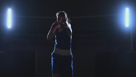 A-beautiful-sports-boxer-woman-in-red-bandages-on-her-hands-and-a-blue-t-shirt-is-fighting-with-a-shadow-practicing-the-speed-and-technique-of-punches.-Camera-movement-side-View.-Steadicam-shot.-Preparing-for-self-defense