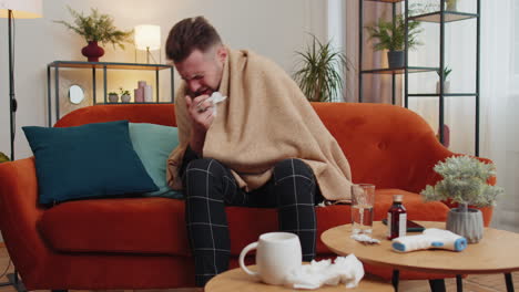 Sick-ill-guy-suffering-from-cold-or-allergy-lying-on-home-sofa-sneezes-wipes-snot-into-napkin