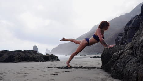 In-slow-motion,-a-young-and-fit-woman-athlete-performs-push-ups-on-a-rock-by-the-ocean