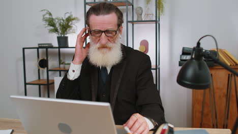 Senior-old-business-man-working-on-laptop-at-office-wearing-earphones-listening-favorite-disco-music