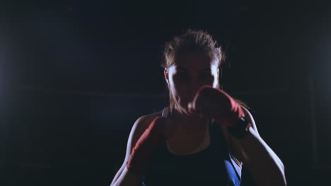 Beautiful-sexy-woman-boxer-dynamically-strikes-directly-into-the-camera-and-moving-forward-on-a-dark-background-with-a-backlight.-Steadicam-shot