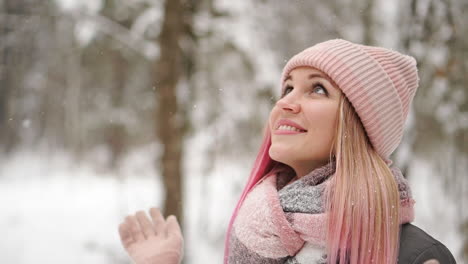 Woman-in-a-jacket-and-hat-in-slow-motion-looks-at-the-snow-and-catches-snowflakes-smiling