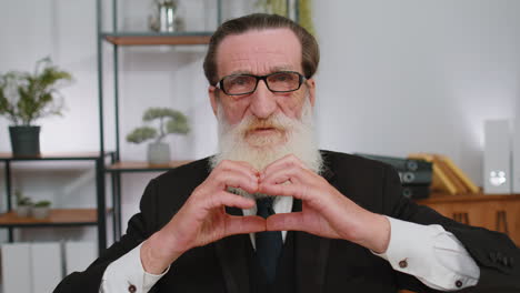 Senior-business-man-makes-symbol-of-love,-showing-heart-sign-to-camera,-express-romantic-feelings