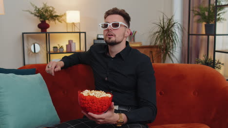 Guy-sitting-on-couch-eating-popcorn-and-watching-interesting-TV-serial,-sport-game-online-at-home