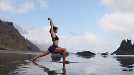 Slow-motion-footage-shows-a-young,-slim-woman-practicing-stretching-and-yoga,-standing-near-the-ocean-and-looking-out-into-the-distance