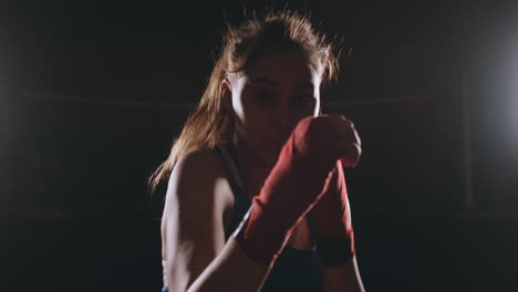Beautiful-sexy-woman-boxer-dynamically-strikes-directly-into-the-camera-and-moving-forward-on-a-dark-background-with-a-backlight.-Camera-moves-Steadicam-shot