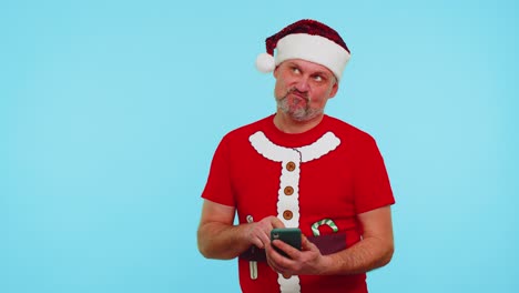 Mann-Mit-Weihnachts-T-Shirt-Und-Hut-Tippt-Mit-Seinem-Mobiltelefon-Einen-Neuen-Beitrag-Im-Internet-Ein,-Kauft-Online-Ein-Und-Stöbert
