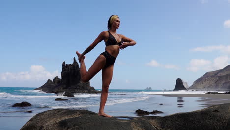 Eine-Junge-Schlanke-Frau-Praktiziert-Yoga,-Während-Sie-In-Zeitlupe-Auf-Einem-Felsen-Am-Meer-Steht