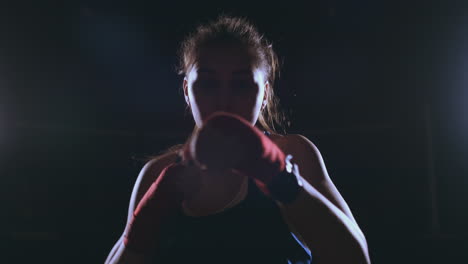 Looking-into-the-camera-a-beautiful-female-boxer-strikes-against-a-dark-background-with-a-backlit-light.-Steadicam-shot