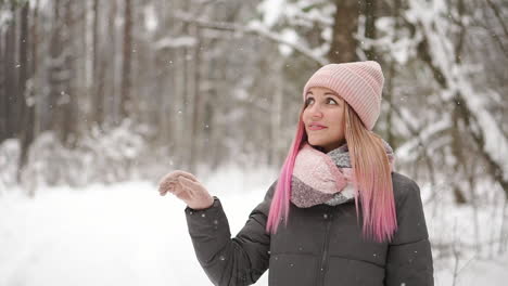 Slow-motion,-winter-woman-in-the-woods-watching-the-snow-fall-and-smiling-looking-at-the-sky-and-directly-into-the-camera.