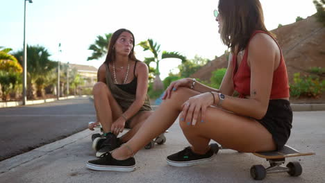 Zwei-Mädchen-Sitzen-Während-Des-Sonnenuntergangs-Auf-Ihren-Skateboards-Im-Skatepark-Und-Sind-In-Gespräche-Vertieft.-Ihr-Lächeln-Und-Lachen-Spiegelt-Die-Kameradschaft-Ihrer-Freunde-Wider.-Ein-Entspannter-Longboard-Chat