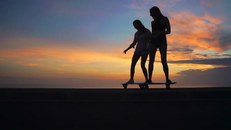 With-a-backdrop-of-mountains-and-a-picturesque-sky,-two-friends-skateboard-on-a-road-at-sunset-in-slow-motion.-Their-attire-includes-shorts