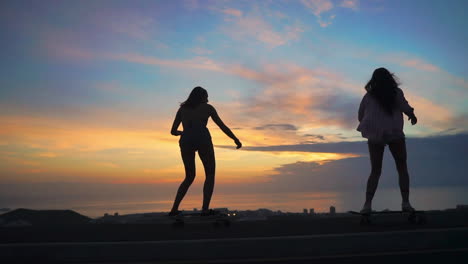 A-sunset-scene-showcases-two-friends-in-slow-motion,-skateboarding-on-a-road-with-mountains-and-a-picturesque-sky.-They're-dressed-in-shorts