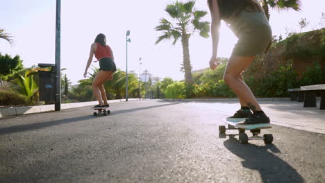 Under-the-sunset,-two-young-Hispanic-women-skateboard-on-an-island,-their-journey-documented-in-slow-motion-along-park-paths.-Celebrating-happiness-and-well-being