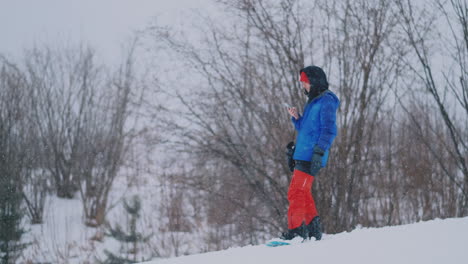 Toma-En-Cámara-Lenta-De-Un-Snowboarder-Usando-Un-Teléfono-Inteligente-Mientras-Conduce-Por-Una-Pista-De-Esquí