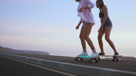 Amid-a-stunning-sunset,-two-friends-skateboard-on-a-road,-with-mountains-and-a-breathtaking-sky-in-the-background.-Slow-motion-recording-highlights-the-scene.-They-sport-shorts