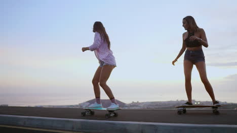 Slow-motion-footage-captures-two-friends-skateboarding-on-a-road-at-sunset,-with-mountains-and-a-stunning-sky-forming-the-backdrop.-They're-wearing-shorts