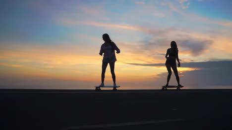 Two-friends-enjoy-slow-motion-skateboarding-along-a-road-during-sunset,-framed-by-mountains-and-a-scenic-sky.-Their-attire-features-shorts