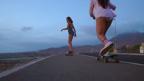 With-mountains-and-a-captivating-sky-in-the-backdrop,-two-friends-engage-in-slow-motion-skateboarding-on-a-road-at-sunset.-They're-dressed-in-shorts