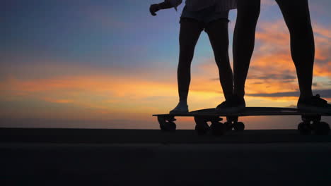 Skateboarding-on-a-road-at-sunset,-two-friends-create-a-mesmerizing-scene-in-slow-motion-with-mountains-and-a-beautiful-sky.-They're-attired-in-shorts
