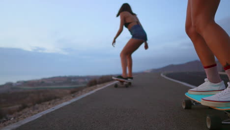 Two-friends-enjoy-slow-motion-skateboarding-on-a-road-at-sunset,-with-the-mountains-and-a-stunning-sky-providing-a-scenic-backdrop.-Shorts-complete-their-attire