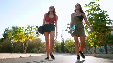 Girls-carry-skateboards-to-the-park-near-palm-trees,-sharing-conversation,-laughter,-and-smiles,-their-camaraderie-illuminated-by-the-setting-sun-in-slow-motion