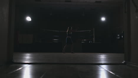 Professional-beautiful-female-boxer-otbryvatyvat-blows-conducting-a-fight-with-a-shadow-in-a-dark-hall-of-the-hall-in-slow-motion-in-blue-clothes-and-red-bandages-on-her-wrists.-zoom-camera.-steadicam-shot