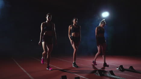 Drei-Mädchen-In-Schwarzer-Kleidung-Stehen-In-Den-Startlöchern,-Um-Im-Licht-Der-Lichter-Das-Rennen-Des-Wettbewerbs-Zu-Starten-Und-In-Richtung-Ziel-Zu-Rennen