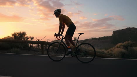 The-athlete-on-a-bike-is-showcased-in-slow-motion-as-he-rides-a-mountain-serpentine,-relishing-the-island's-view,-symbolizing-a-dedication-to-a-healthy-lifestyle-during-sunset