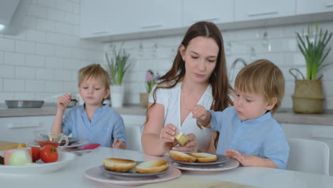 Beautiful-young-mother-with-two-children-sons-on-white-light-kuna-cook-with-burgers