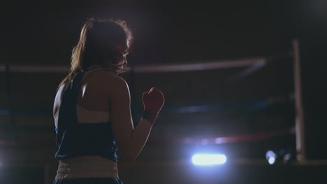A-beautiful-woman-conducts-a-shadow-fight-while-practicing-hard-for-future-victories.-Dark-gym-background.-steadicam-shot