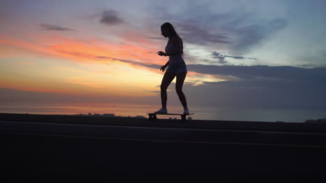 Schönes-Mädchen-Fährt-Auf-Der-Straße-Auf-Einem-Skateboard-Gegen-Den-Sonnenuntergangshimmel
