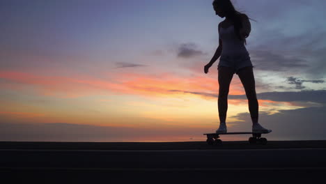 Schönes-Mädchen-Fährt-Auf-Der-Straße-Auf-Einem-Skateboard-Gegen-Den-Sonnenuntergangshimmel