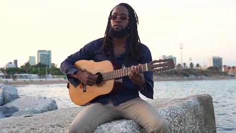 African-American-musician-playing-guitar-on-coast-near-city
