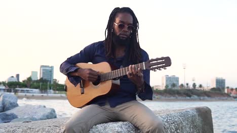 African-American-musician-playing-guitar-on-coast-near-city