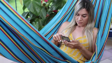 Woman-browsing-smartphone-and-resting-in-hammock