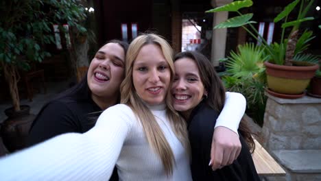 Cheerful-girlfriends-embracing-while-taking-selfie-in-bar
