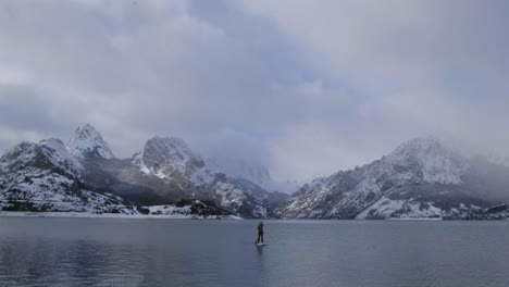 Man-on-paddle-board-between-water-and-mountains-on-coast