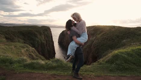 Man-lifting-woman-on-cliff-near-sea