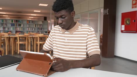 Schwarzer-Student-Macht-Hausaufgaben-Mit-Tablet-In-Der-Bibliothek