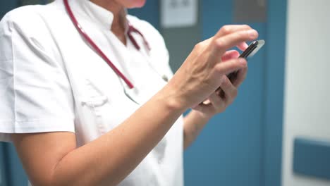 Cheerful-pediatrician-using-smartphone-in-hospital-hallway