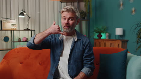 Mature-man-looking-at-camera-advertising-doing-phone-gesture-like-says-hey-you-call-me-back-at-home