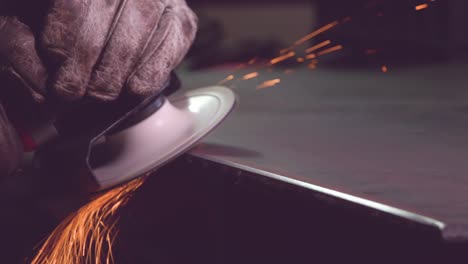 Crop-metal-worker-in-gloves-grinding-edge-of-metal-handiwork