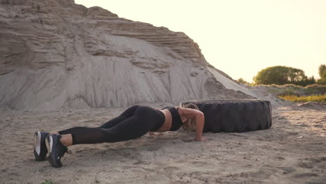 Girl-on-sand-quarry-jumping-burpee-with-push-UPS-through-the-wheel-in-the-sand