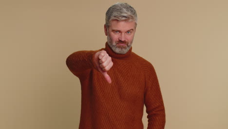 Upset-senior-man-guy-in-sweater-showing-thumbs-down-sign-gesture,-disapproval,-dissatisfied-dislike
