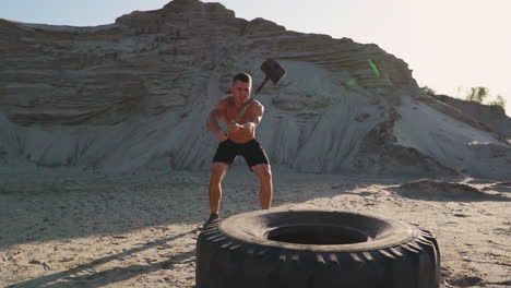 Muscle-athlete-strongman-man-hits-a-hammer-on-a-huge-wheel-in-the-sandy-mountains-in-slow-motion.-strength-and-endurance-training-for-wrestlers